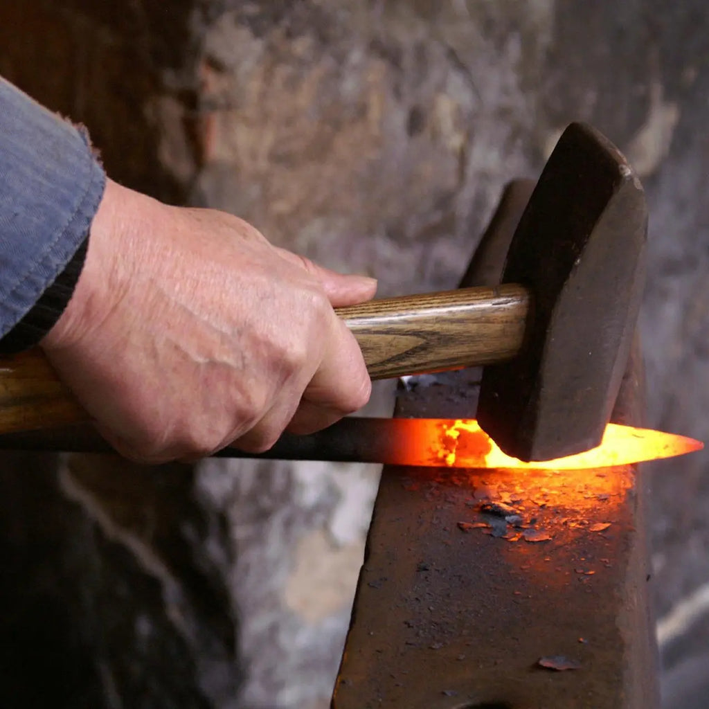 Herrero en taller forja producto de metal en yunque con martillo